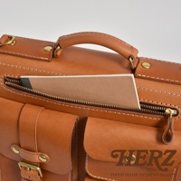 職人手作皮革三口袋三用後背包，採用棕色皮革製成，設有拉鍊開口，內有筆記本，外部有兩個帶有金屬釦的口袋，以及一個手提握把。