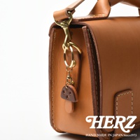 職人手作皮革香菇造型鑰匙圈，採用天然皮革製成，香菇造型為深棕色，傘蓋上有兩個小圓孔，搭配金色鑰匙圈與登山扣。