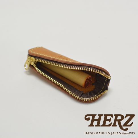 職人手作皮革印章收納袋，淺棕色皮革，拉鍊式開合，內部收納一個圓柱形印章。