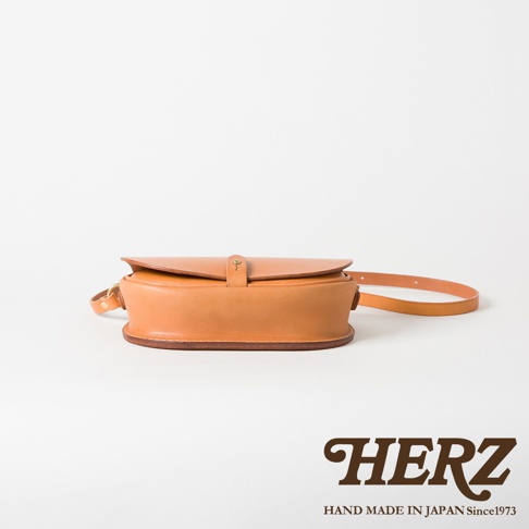 職人手作皮革迷你馬鞍包，採用經典馬鞍造型，全皮革製成，淺棕色。包身呈現自然的皮革紋理，配有可調節的細長肩帶和金屬釦設計。