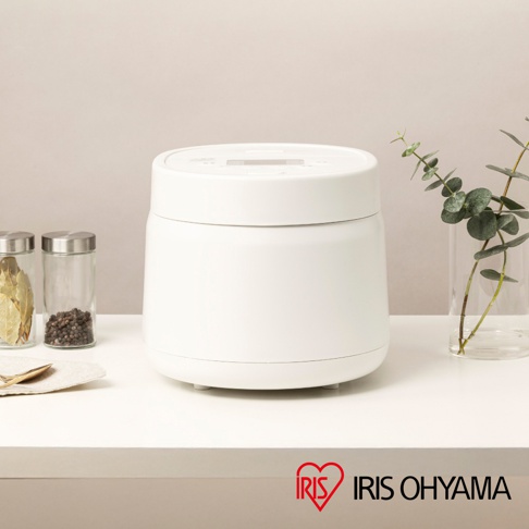 白色電鍋，旁邊有兩個裝有香料的玻璃罐，角落有兩個綠葉的裝飾，底部有IRIS OHYAMA的紅色愛心Logo。