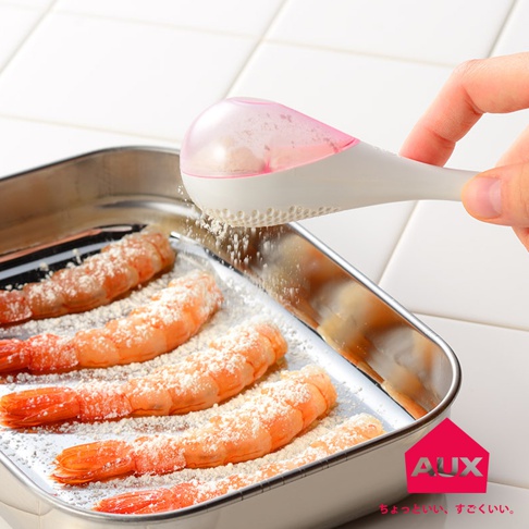 手持白色帶粉紅色半透明蓋子的leye料理專用撒粉器，正將白色細粉均勻撒在不銹鋼烤盤中的鮮蝦上。
