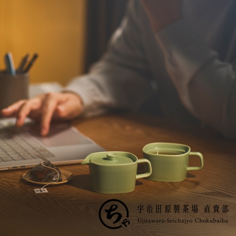 一位使用者坐在木桌前使用筆記型電腦，桌面上擺放著一組淡綠色的美濃燒一人用茶壺與茶杯，旁邊還有一袋茶包。圖片下方印有宇治田原製茶場直賣部的品牌標誌與文字。