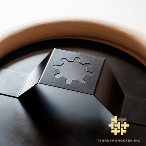 wawa藤編圓鏡的近距離特寫，展示了黑色金屬支架，其上方有一個雪花狀鏤空設計，支架固定在圓形鏡子的黑色背板上，鏡子邊緣露出部分淺棕色編織邊框。