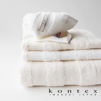 堆疊的白色今治雙織有機棉浴巾，頂部浴巾上有「Organic cotton 100%」標籤。浴巾呈現鬆餅格紋織紋，質地柔軟。