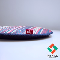 天然藺草紋織圓型坐墊，表面有粉紅色、藍色、白色相間的幾何圖紋，側邊為深藍色牛仔布包邊，並附有紅色品牌標籤。