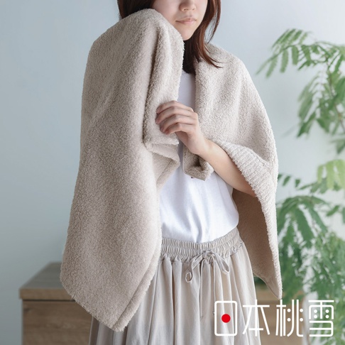 女性身著一條米白色浴巾，搭配同色系的長裙，背景為綠色植物和木質櫃子，右下角有「日本桃雪」的標誌。