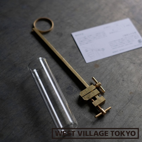 黃銅製的長柄夾具，末端帶有可調節的夾子，夾住一支透明玻璃試管，旁邊放著一張白色小卡片。