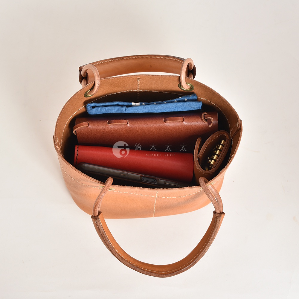 淺棕色皮革大開口提把午餐袋，內部裝有藍色布料、棕色皮革夾、紅色長夾和手機。