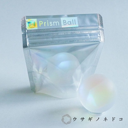 霧面合光稜鏡球，半透明的霧面質感，在光線下呈現彩虹般的光澤，其中一顆置於透明展示台上。