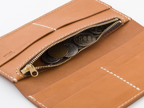 淺棕色皮革長夾，內部拉鍊零錢袋中裝有日圓硬幣，精緻的縫線勾勒出簡約的設計。