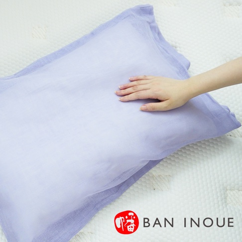 淡紫色兩層蚊帳棉織親膚枕套，一隻手輕撫枕套表面，枕套放置於白色紋理床墊上，右下角有品牌標誌。