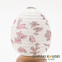 一個白色的紙質提燈，上面印有粉紅色的兔子、花朵和刺蝟圖案，提燈頂部有金屬掛環，下方由木製底座支撐。