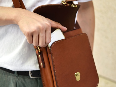 職人手作皮革翻蓋迷你單肩包，採用棕色牛皮製作，配有金色金屬扣環。包包設計簡約，翻蓋式開合，可放入手機，展現皮革質感與精緻工藝。