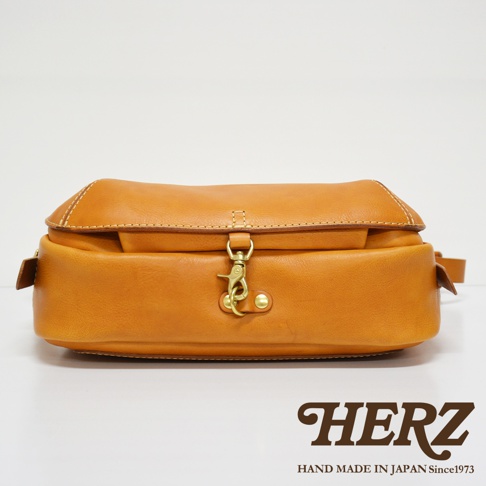 職人手作皮革復古翻蓋郵差包，淺棕色皮革材質，配有黃銅色金屬扣環及旋轉鎖，簡約設計，適合日常攜帶。