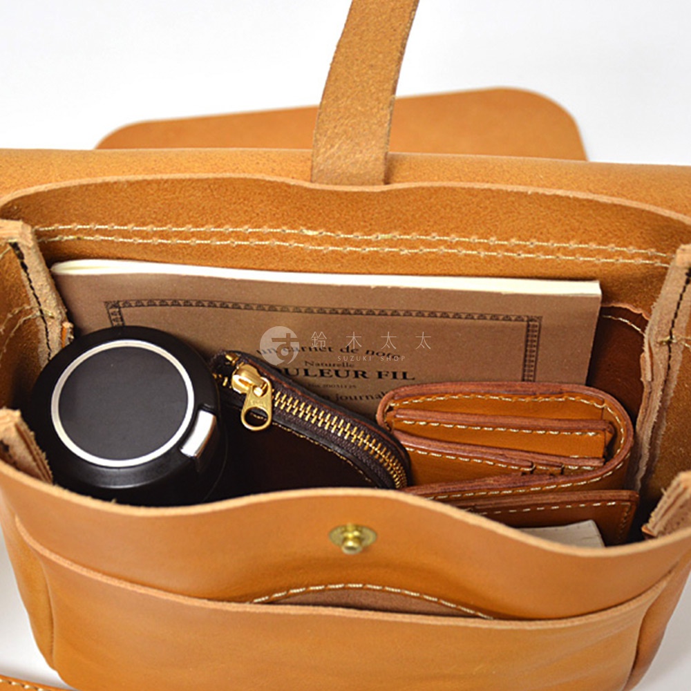 一個手工皮革斜背包，裡面有筆記本、化妝盒和錢包。