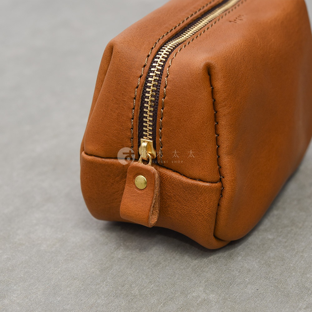 一個日本HERZ職人手作的棕色皮革收納包特寫，展示了精緻的縫線細節、復古金屬拉鍊以及帶有黃銅鉚釘的皮革拉鍊拉環，整體呈現溫潤的皮革質感與簡約設計風格。