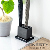 黑色珪藻土可拆式六孔傘架，簡約方形設計，搭配灰色與黑色摺疊傘，旁邊有一個灰色盆栽，整體呈現現代居家風格。