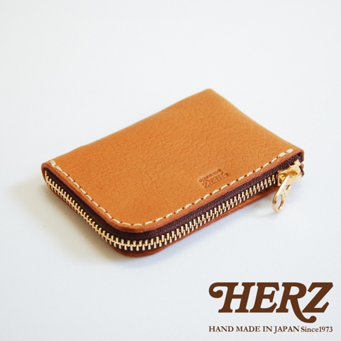 日本HERZ職人手作棕色皮革L型拉鍊卡片收納夾，採用柔軟牛皮材質，具備質感鮮明的紋理與白色粗縫線細節，搭配金色拉鍊與日本手工製造品質，底部右側壓印HERZ品牌字樣，整體呈現簡約俐落的皮革小物設計。
