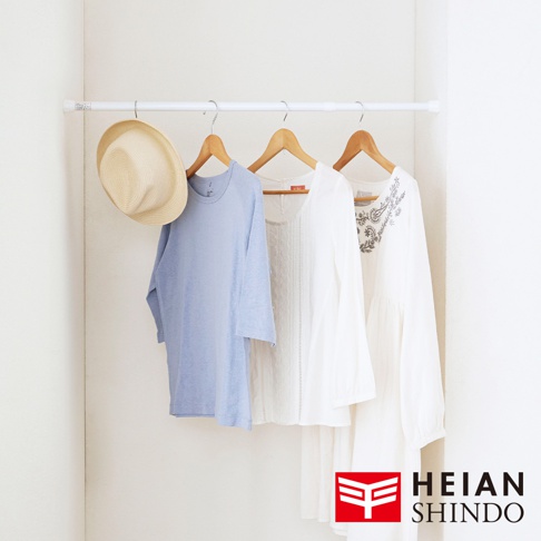 白色伸縮桿上掛著一頂草帽，以及一件淺藍色長袖上衣、一件白色蕾絲上衣和一件白色刺繡長袖洋裝。