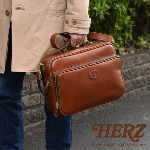 棕色皮革製成的兩用商務公事包，帶有頂部提把和可拆卸肩帶，前面有一個拉鍊口袋，上面有圓形皮革標誌。