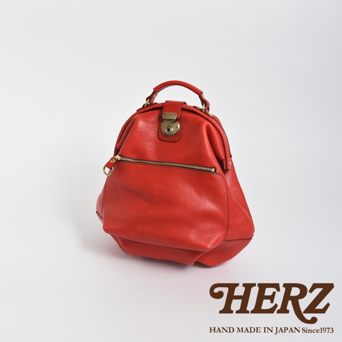 職人手作皮革輕旅行後背包 R-144，採用紅色牛皮製成，包身圓潤，設有金色金屬鎖扣、拉鍊前袋及提把，風格復古。