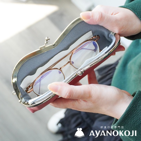 一雙金屬框眼鏡被放入綾織帆布製成的京都職人手作口金眼鏡收納盒，收納盒外部為紅色，內部襯有灰色布料，盒蓋處有金屬開合扣，圖片底部有品牌LOGO和日文名稱「がま口の専門店 AYANOKOJI」。