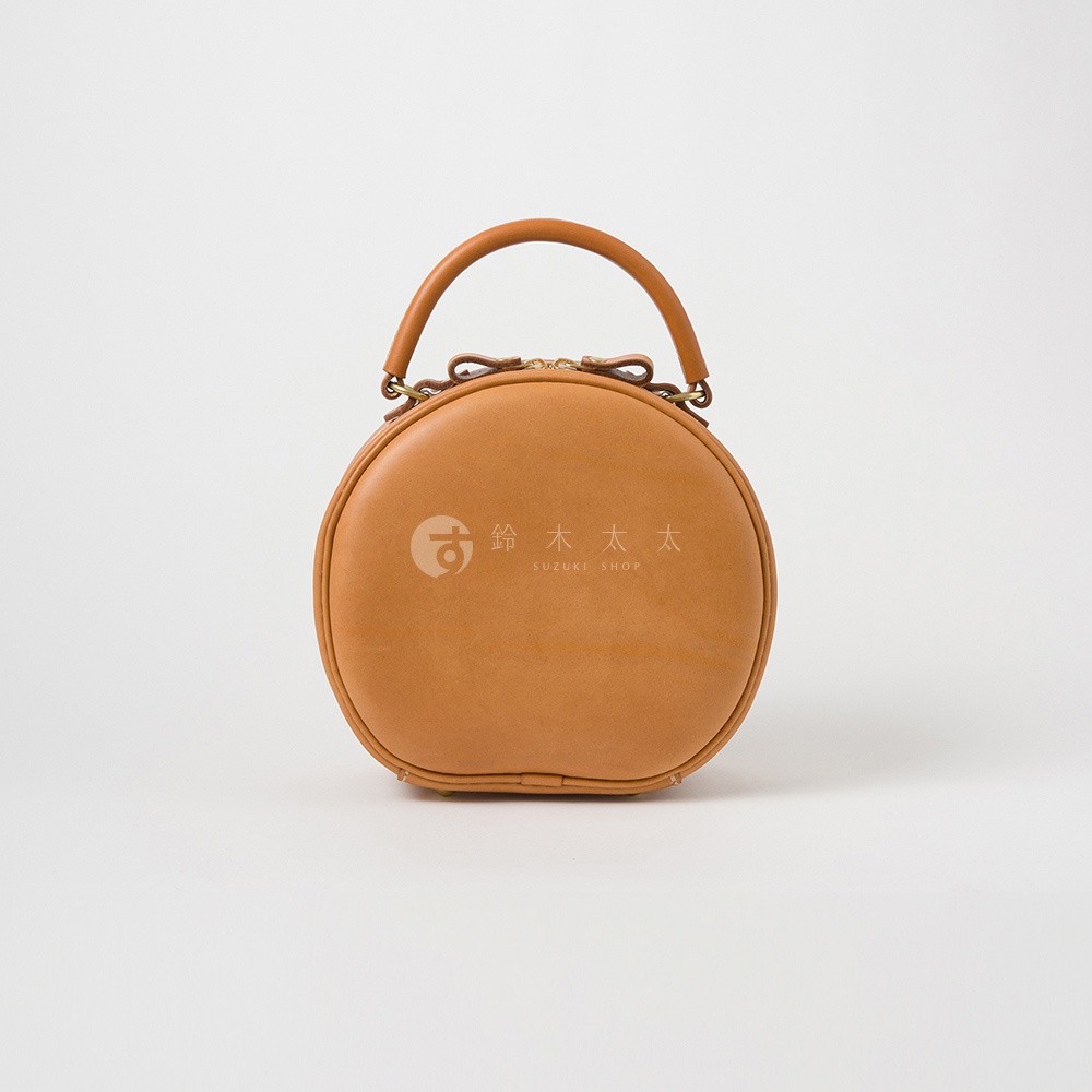 一個淺棕色皮革製成的圓形手提包，上面有一個提把，包包正面有SUZUKI SHOP的標誌。
