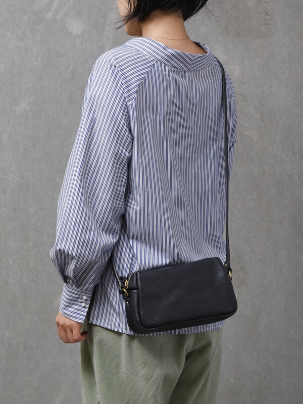 黑色皮革輕巧拉鍊單肩包，配有金色金屬配件和可調節肩帶，以側身展示。