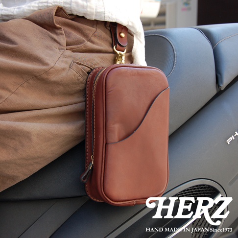 日本HERZ職人手作皮革兩用直立型斜背包，展示於機車座椅上，標誌為「HERZ HAND MADE IN JAPAN Since1973」。