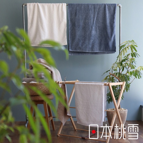 三條不同顏色的精梳棉浴巾，一條為米白色，另一條為深藍色，掛在金屬架上；下方木製架上掛著一條淺米色浴巾，旁邊籃子裡疊著幾條深淺不一的毛巾。