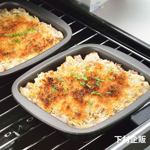 兩個深灰色、帶有烤至金黃色酥脆頂層的迷你方形烤盤，烤盤內盛有似乎是馬鈴薯泥與肉末混合的焗烤料理，並撒上切碎的綠色香料。