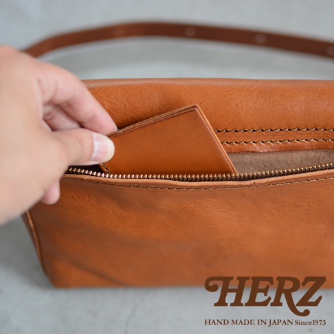 特寫鏡頭展示了一隻手將一張卡片放入手工製作的棕褐色皮革包的拉鍊口袋中。