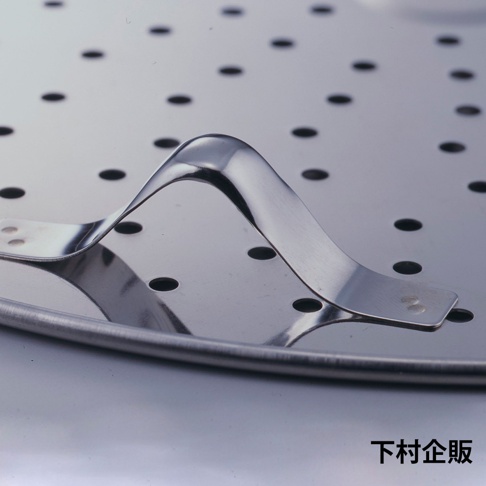 銀色金屬製的平底鍋專用萬用蒸盤，盤面佈滿圓形孔洞，中央設有彎曲狀的金屬提把，提把透過铆釘固定在蒸盤上，整體呈現光澤。