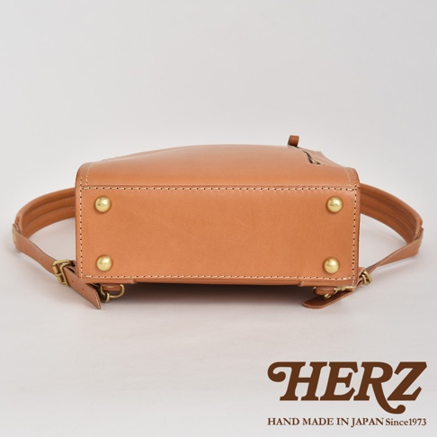 一張特寫圖，顯示職人手作皮革商務電腦後背包 R-25 的底部及部分側面。後背包為經典的駱駝色皮革，帶有精緻的縫線和黃銅色的鉚釘裝飾。