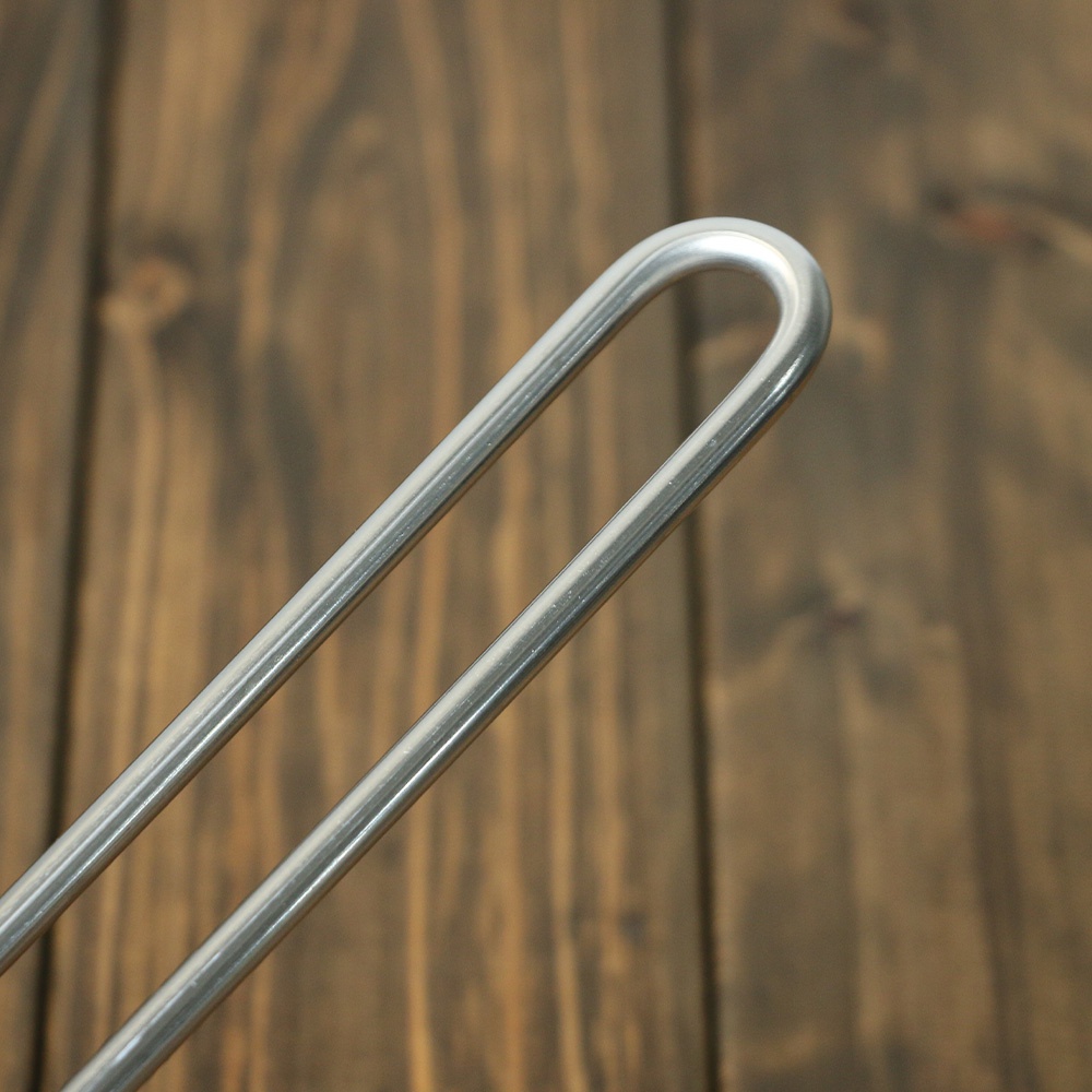 不鏽鋼雙口牛奶鍋的鍋柄，呈現銀色金屬光澤，由兩條弧形不鏽鋼桿構成，置於深棕色木紋背景上。