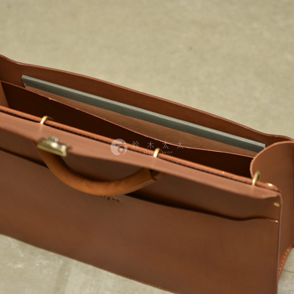 職人手作的棕色皮革公事包，內部可見隔層與一個灰色文件夾，包款設有提把及金屬鎖扣，展現簡潔的商務風格。