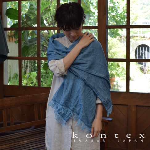 藍色微透輕柔羊毛棉質混紡絲巾，以寬鬆方式披在身上，絲巾邊緣帶有流蘇，質料輕薄。