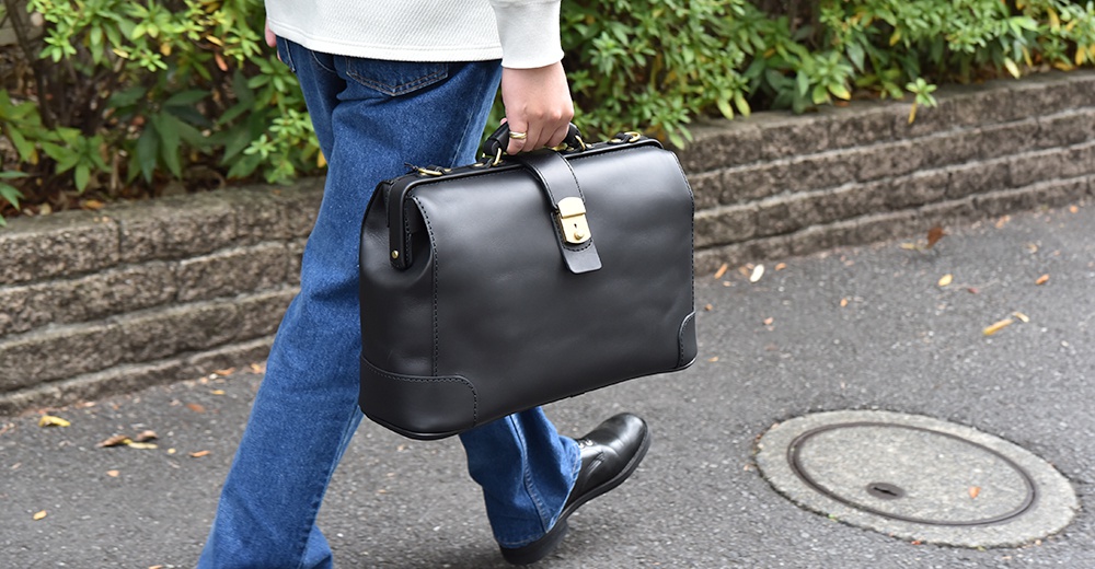 黑色皮革公事包，帶有金色旋鎖扣和頂部提把，適合商務旅行。