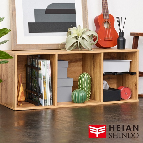 木紋色調的層架式收納櫃，內有雜誌架、書籍、綠色裝飾品、灰盒、白色收納盒、紙巾盒及紅色時鐘，櫃頂擺放盆栽與紅色烏克麗麗。