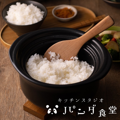 Kitchen Studio Panda食堂 萬古燒職人炊飯土鍋，內盛飽滿的白米飯，木製飯勺置於其中，旁有小碟醃漬物及一盤什錦蔬菜。