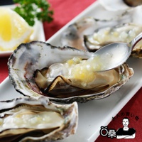 生蠔盛裝在白色盤中，盤邊可見檸檬塊和綠色香草。其中一顆生蠔正被銀色湯匙舀起，湯匙上沾有黃色醬料。生蠔外殼呈現灰白色，內部肉質肥美。