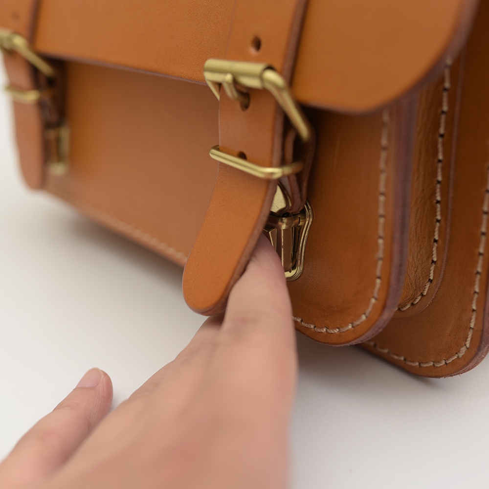 職人手作皮革雙扣兩用迷你肩背包，展現天然皮革的溫潤質感，搭配金色雙扣環設計，簡潔而精緻，適合日常攜帶。