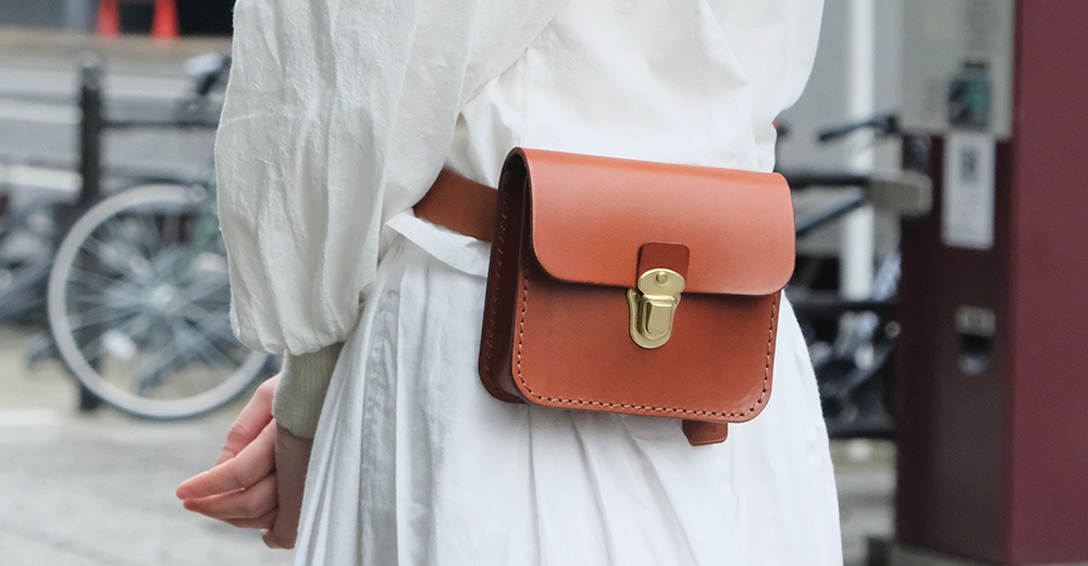 棕色皮革經典腰包，附有金色金屬鎖扣，由皮革製成，縫線精緻，可繫於腰間。