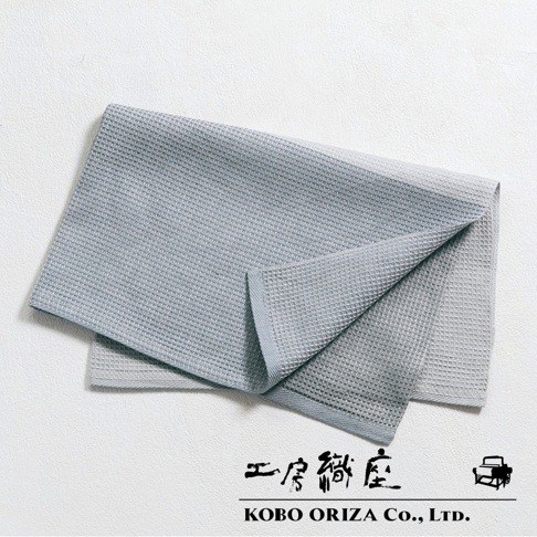 淺灰色棉麻混紡拭巾，具有標誌性的鬆餅紋理，一角向內摺疊，露出內裡的淺灰色。