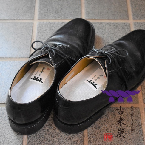 一雙黑色皮鞋，鞋內各置有印有日文標誌的白色鞋墊。