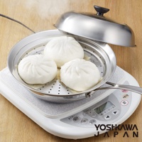 不鏽鋼蒸鍋盤置於電磁爐上，盤內有三個白色包子，蒸鍋配有透明蓋，盤身及鍋蓋材質為不鏽鋼。