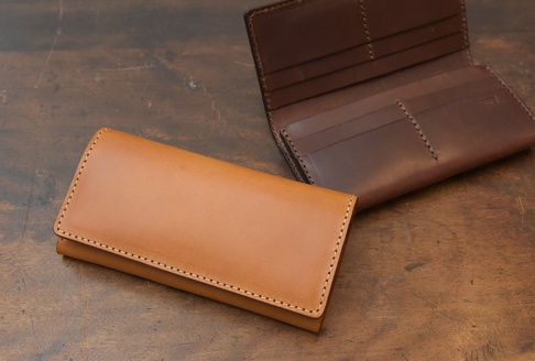 兩個職人手作皮革長夾，一個為淺棕色、閉合狀態，另一個為深棕色、展開狀態，露出多個卡片夾層。