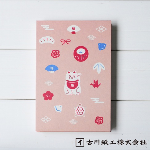 粉紅色和紙御朱印帳，印有各種吉祥圖案，包括招財貓、達摩、扇子、花朵、烏龜、千羽鶴和日式紋樣，圖案顏色為白色、紅色和藍色。