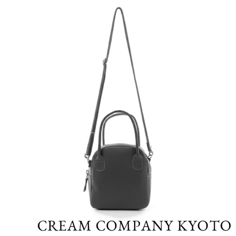 由京都品牌 CREAM COMPANY KYOTO 設計的手作牛皮貝殼包，呈現簡約圓潤的直立式結構，設有雙提把與可拆式肩背帶，包身選用耐用皮革材質，底部標示品牌名稱。